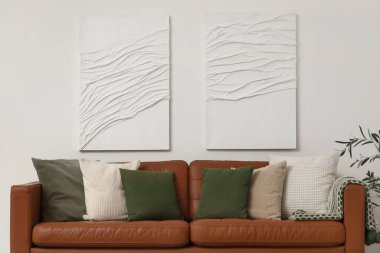 Oturma odasındaki beyaz duvarın yanında yumuşak yastıklı kahverengi deri kanepe.