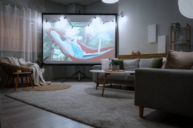 Gri koltukları, kahve masası ve modern projektör ekranı olan şık bir oturma odası.