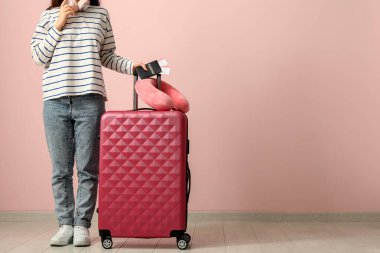 Pembe duvarın yanında bavulu, seyahat yastığı ve pasaportu olan genç bir kadın.