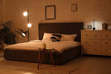 Büyük yataklı, parlak lambalı ve beyaz tuğlalı duvarın yanında klozeti olan bir gece odası.