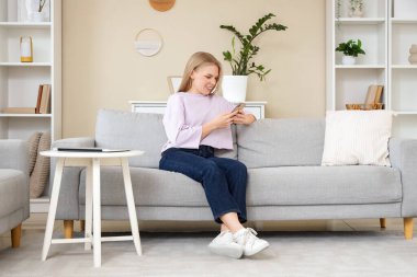 Evdeki koltukta cep telefonu kullanan genç sarışın kadın.