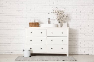 Çiçek açan dalları olan vazolar ve banyonun içindeki beyaz tuğla duvarın yanındaki çekmecelere batıyor.