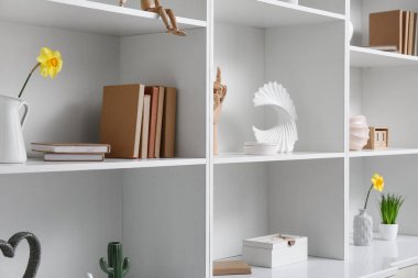 Beyaz raflardaki vazolarda kitap ve nergislerle süslü bir dekor.