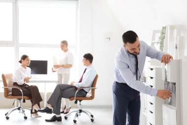 Genç işadamı ofisteki soğutucudan su dolduruyor