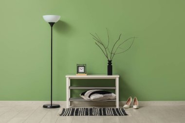 Bankta ve yerde lamba, odanın içindeki yeşil duvarın yanında.