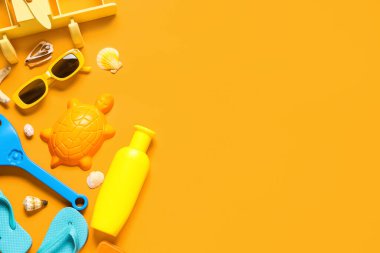 Kum kalıplı kompozisyon, bir şişe güneş kremi ve turuncu arka planda plaj aksesuarları.