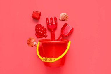 Kumsal kumları, deniz kabukları, oyuncak tırmık, kürek ve kovayla kırmızı arka planda kompozisyon