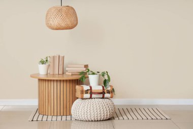 Masa, puf, kitaplar ve ev bitkileri odanın içindeki bej duvarın yanında.