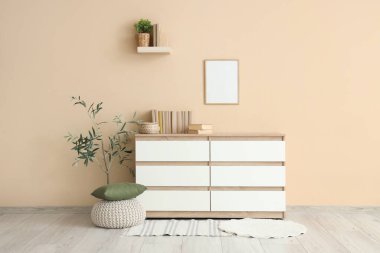 Odanın iç tarafındaki bej duvarın yakınındaki çekmecelerin üzerindeki sandık ve kitaplar.