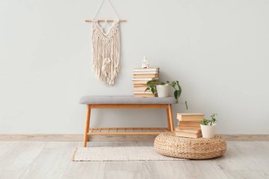 Bank, puf, kitaplar ve ev bitkileri odanın içindeki beyaz duvarın yanında.