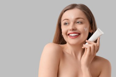 Yüzünde güneş kreminden yapılmış bir kalp ve gri arka planda bir tüp olan güzel bir genç kadın.