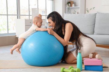 Evde küçük bebeğiyle spor yapan genç bir kadın.