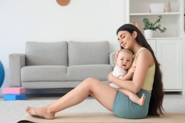 Küçük bebeğiyle evde yoga minderinde oturan sportif bir anne.