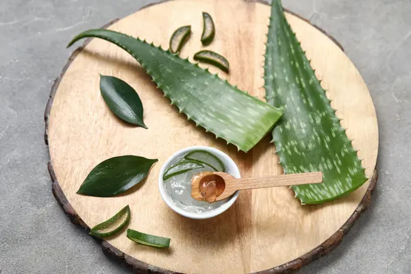 Bir kase aloe vera jeli ve gri arka planda yaprakları olan ahşap tahta.