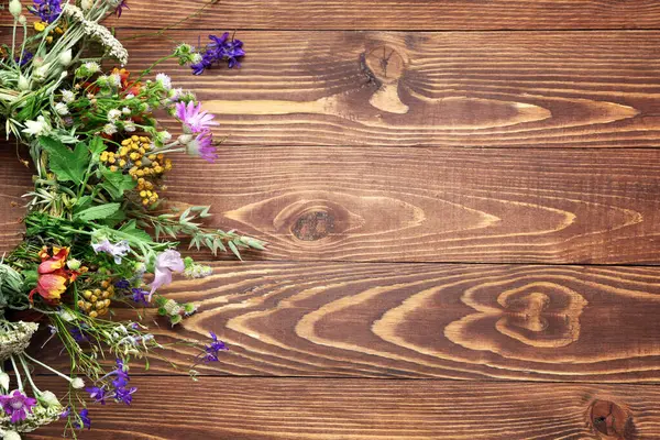 Kahverengi ahşap arka planda güzel kır çiçeklerinden yapılmış çelenk, yakın plan. Yaz gündönümü