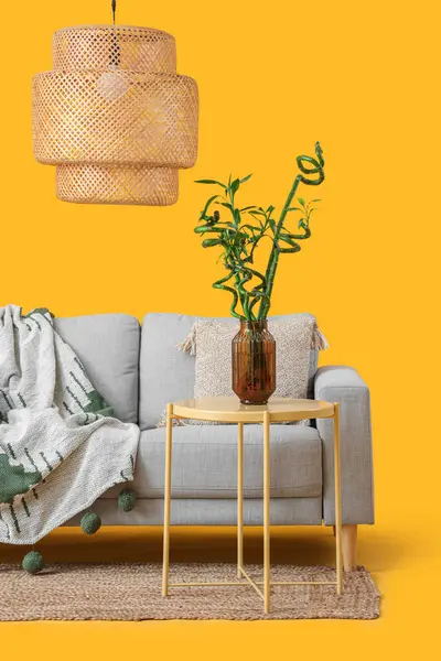 Vazoda bambu saplı masa, kanepe ve sarı arka planda lamba.