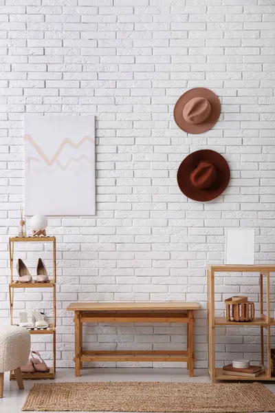 Raflar, bank ve ayakkabılar koridorun iç tarafındaki beyaz tuğla duvarın yanında duruyor.