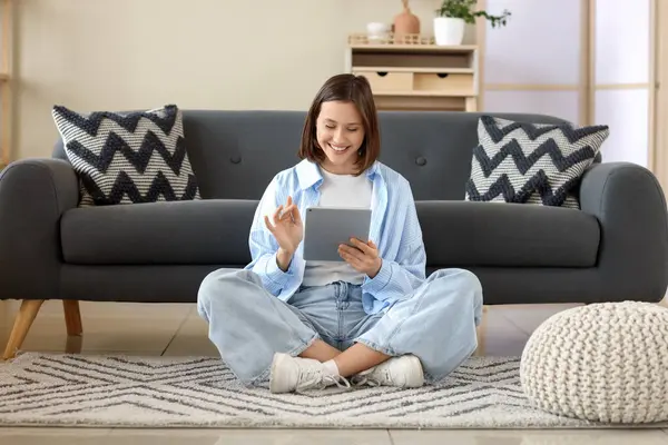 Evdeki halının üzerinde modern tablet bilgisayar kullanan genç bir kadın.