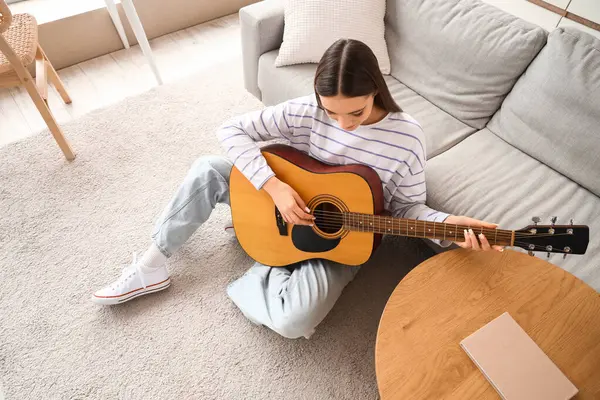 Evde gitar çalan genç bir kadın.