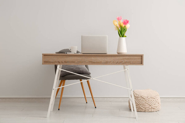 Stylish workspace with modern laptop and beautiful flowers near white wall