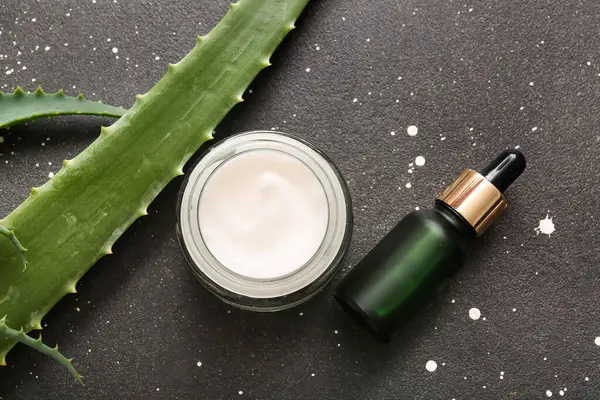 Bir şişe kozmetik yağı ve siyah arka planda aloe vera yapraklı bir kavanoz krema.