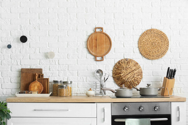 Стол с плитой и посудой рядом с белой кирпичной стеной на кухне