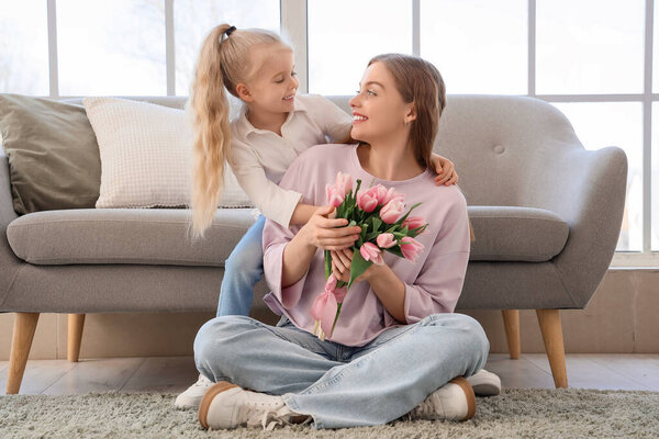 Милая маленькая девочка поздравляет свою маму с Днем матери тюльпанами в гостиной
