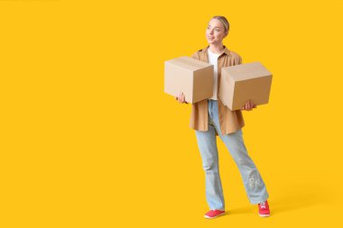Sarı arka planda paket kutuları olan genç bir kadın.