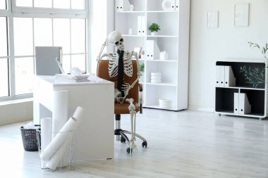 Ofisteki masasında düşünceli insan iskeleti modeli.