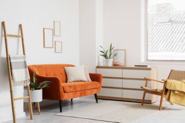 Beyaz duvarın yanında rahat kahverengi kanepesi ve merdiveni olan modern oturma odası.