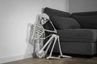 Odadaki kanepenin yanında oturan üzgün insan iskeleti modeli.
