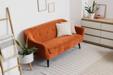 Beyaz duvarın yanında rahat kahverengi kanepesi ve merdiveni olan modern oturma odası.