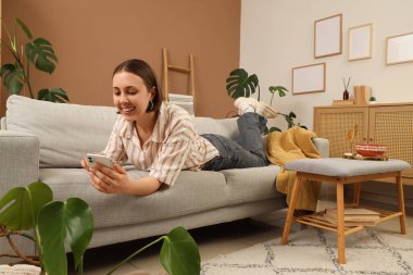 Oturma odasındaki koltukta cep telefonu kullanan genç bir kadın.