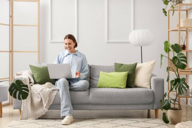 Oturma odasındaki kanepede dizüstü bilgisayarla çalışan genç bir kadın.