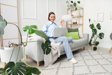 Oturma odasındaki kanepede dizüstü bilgisayarla çalışan genç bir kadın.