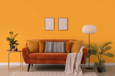 Rahat kahverengi kanepe ve oturma odasının iç tarafındaki sarı duvarın yanındaki bitkiler.