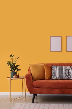 Rahat kahverengi kanepe ve oturma odasının iç tarafındaki sarı duvarın yanındaki masa.