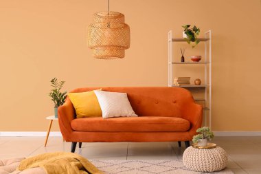 Konforlu kahverengi kanepe, puf ve raf ünitesi odanın içindeki bej duvarın yanında.