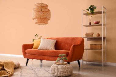 Konforlu kahverengi kanepe, puf ve raf ünitesi odanın içindeki bej duvarın yanında.