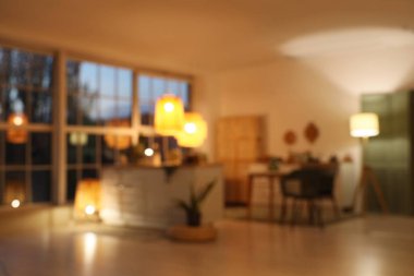 Modern mutfak manzarası bulanık tezgahlar, yemek masası ve akşamları parlayan lambalar.