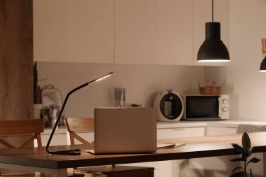 Geceleri mutfaktaki masada parlayan lambalı dizüstü bilgisayar.