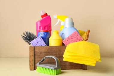 İçinde temizlik malzemeleri ve bej arka planda bir şişe deterjan olan bir kutu.