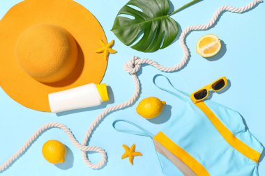 Mavi arka planda mayo, plaj aksesuarları, limonlar ve tropikal yaprak kompozisyonu