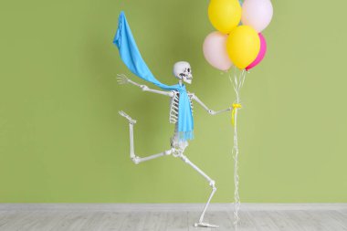 Yeşil duvarın yanında balonlar olan atkılı iskelet