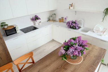 Masası, tezgahı ve leylak çiçekleri olan aydınlık mutfağın içi.