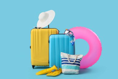 Mavi arka planda plaj aksesuarları olan bavullar.