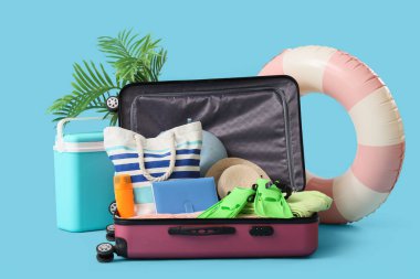 Mavi arka planda giysi ve plaj aksesuarları olan bavul.