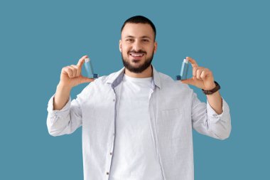 Mavi arka planda astım spreyi olan genç bir adam.