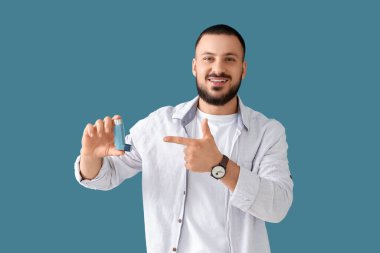 Mavi arka plandaki astım spreyini gösteren genç adam.