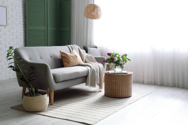 Oturma odasının içinde çiçek açan leylak dalları olan kanepe ve hasır sehpa.